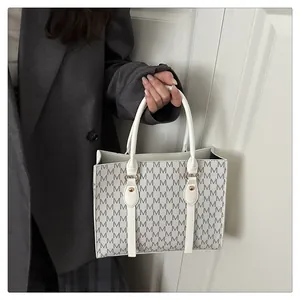 Close-up of white monogram tote bag with gold studs on gray blazer background