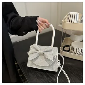 Détail du sac de soirée à paillettes argentées avec grand nœud et poignée blanche
