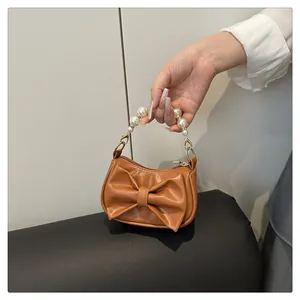 Close-up of caramel brown mini bag with faux pearl handle and large decorative bow detail