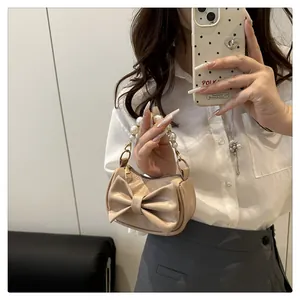 Mini beige tote bag with a large bow and pearl handle shown in a mirror selfie