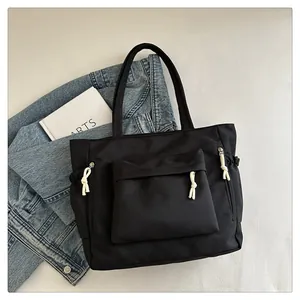 Close-up of black nylon tote bag with large front pocket and white woven rope zipper pulls