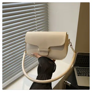 Detail of cream white handbag featuring a thick round handle and gold chain link accents