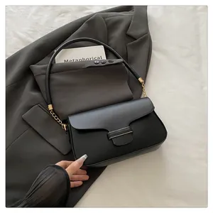 Flat lay of black minimalist flap handbag with gold metal hardware on gray blazer