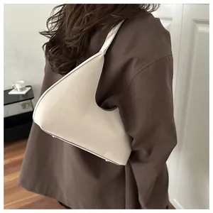 Detail einer beige Halbmond-Schultertasche mit asymmetrischem Design und Metallnieten