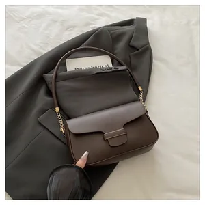 Close-up of brown leather flap handbag on a grey suit jacket with gold chain strap detail
