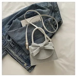 Détail de sac à main argenté brillant avec nœud posé sur une veste en jean et bandoulière