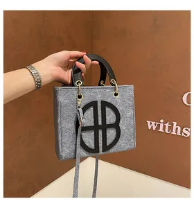 Détail d'un sac cabas en feutre gris avec logo en cuir noir et bandoulière amovible