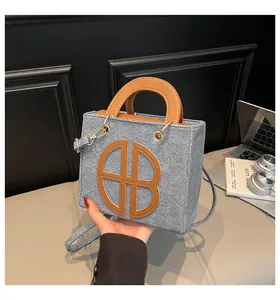 Détail du sac à main en jean bleu clair avec anses en cuir marron et logo surpiqué