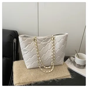 Detailed macro of white quilted faux leather texture and gold chain strap on tote bag