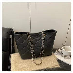 Detail of black quilted tote bag featuring gold chain straps on a cozy beige knit mat