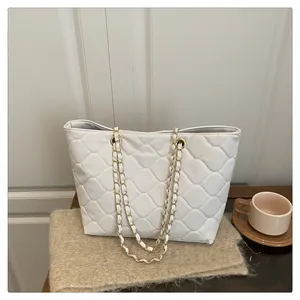 Detail of white quilted tote bag with gold chain strap on a cozy wooden table