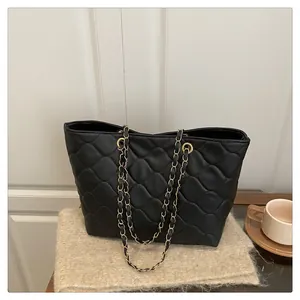 Detail of black quilted leather tote bag with gold metal chain straps on beige knit background