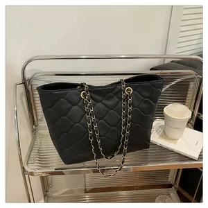 Close-up of black quilted tote bag with gold chain strap on a silver display shelf