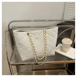 Detail of white quilted tote bag with golden metal chain strap on minimalist shelf