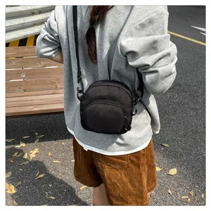 Close-up of a black nylon crossbody bag with adjustable strap in an autumn street setting