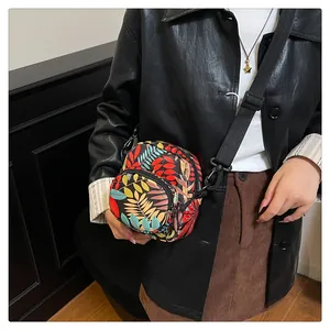 Close-up of small crossbody bag with colorful tropical leaf pattern and adjustable strap