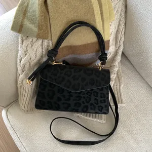 Detail of leopard print handbag with knotted handle and gold hardware on white sofa
