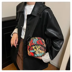 Model wearing a black floral print crossbody bag with adjustable strap and zippers