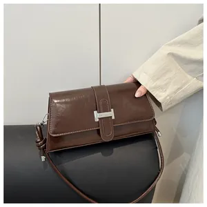 Detail of dark brown glossy leather shoulder bag featuring a silver square metal buckle