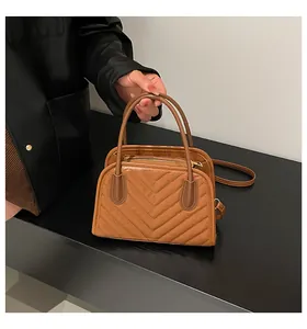 Detail of caramel brown quilted handbag featuring V-pattern stitching and sturdy top handles