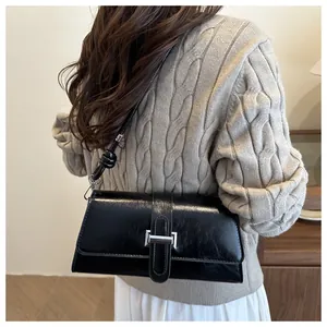 Close-up of black glossy leather shoulder bag with silver buckle on a knitted sweater