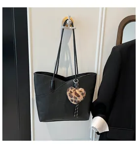 Detail of black pebbled leather tote bag featuring a leopard print heart plush charm