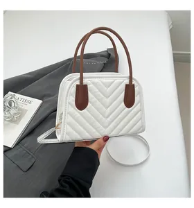 Close-up of white quilted handbag with brown handles and V-shaped stitching details