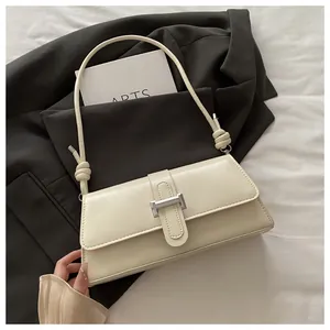 Detail of cream baguette bag featuring a silver buckle and knotted shoulder strap