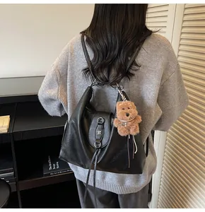 Detail of black leather multi-way hobo bag with floral metal clasp and plush bear charm