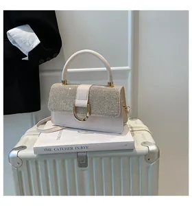 Detail of elegant cream handbag with gold clasp resting on a book and suitcase