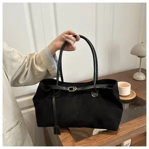Close-up of minimalist black suede tote bag with gold buckle and elegant leather handle
