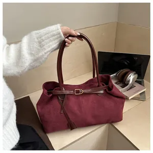 Detail of burgundy suede tote bag featuring brown leather handles and golden buckle decor