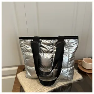 Detail of silver quilted tote bag featuring metallic gloss fabric and black woven handles