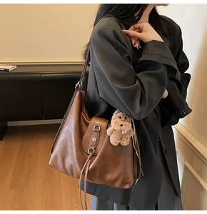 Detail of caramel brown hobo bag with floral metal buckle, tassels and plush bear charm