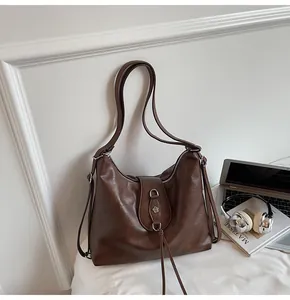 Detail of dark brown leather hobo bag with floral metal logo and decorative long tassels
