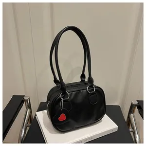 Dettaglio borsa a mano in pelle nera con grana litchi e ciondolo a forma di cuore