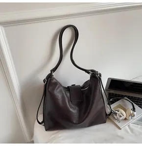 Detail of dark brown leather tote bag with thin straps and zipper on a white surface