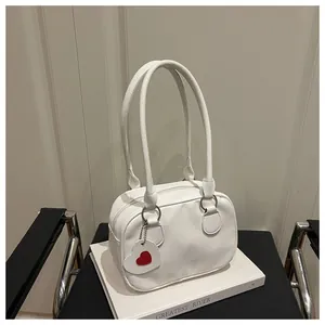 Dettaglio borsa bianca in pelle martellata con ciondolo a cuore rosso su sedile nero