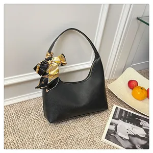 Close-up of black lychee leather crescent bag with decorative printed silk scarf on handle