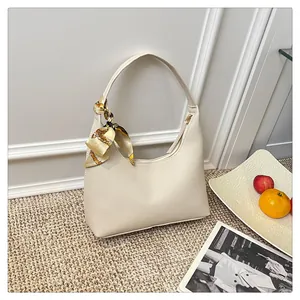 Close-up of beige crescent bag in lychee leather featuring a decorative silk scarf
