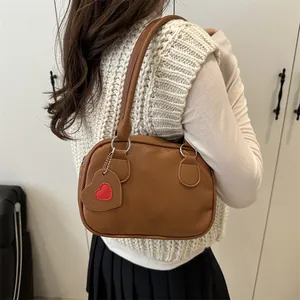Borsa a mano minimalista in pelle marrone caramello con ciondolo a cuore sulla spalla
