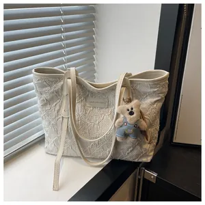 Dettaglio ricamo floreale su borsa tote crema con ciondolo a orsetto e etichetta in pelle