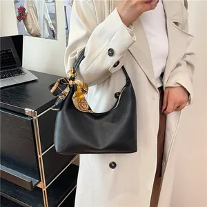 Women's black pebbled crescent shoulder bag with silk scarf on a beige trench coat