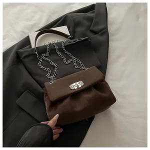 Détail du sac bandoulière en daim marron foncé avec fermoir floral argenté et chaîne en métal