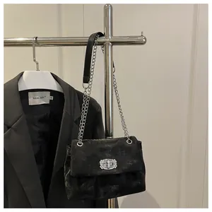 Détail d'un sac à main en velours noir avec un fermoir à strass et une bandoulière chaîne