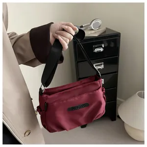 Detail of burgundy nylon crossbody bag with adjustable wide strap and pleated side design