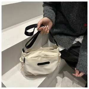 Close-up of minimalist cream nylon crossbody bag featuring functional zippers and side pockets