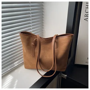 Detail of a large tan suede tote bag with slim shoulder straps on a sunlit window sill