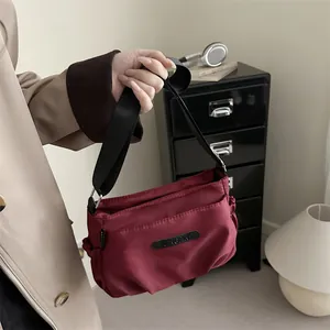 Minimalist burgundy nylon crossbody bag featuring a branded patch and wide shoulder strap
