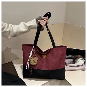 Primer plano de un elegante bolso tote bicolor burdeos y negro con llavero de oso.